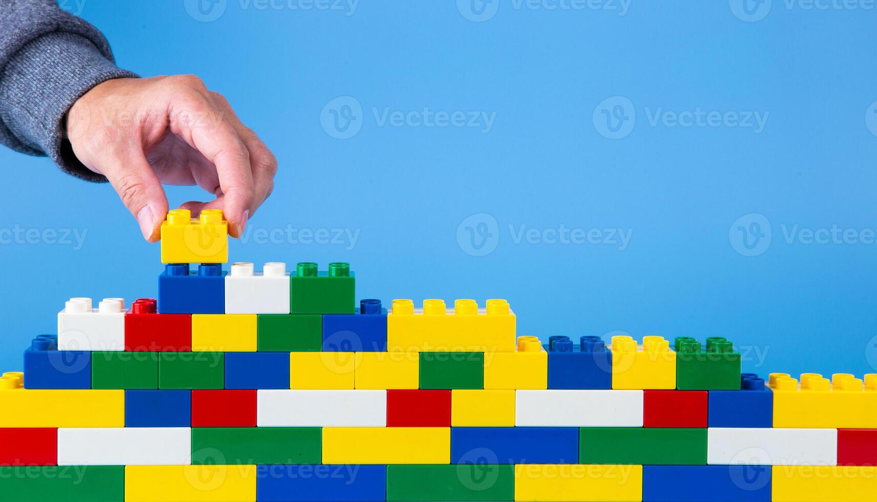 hand building up a wall by stacking up plastic block photo