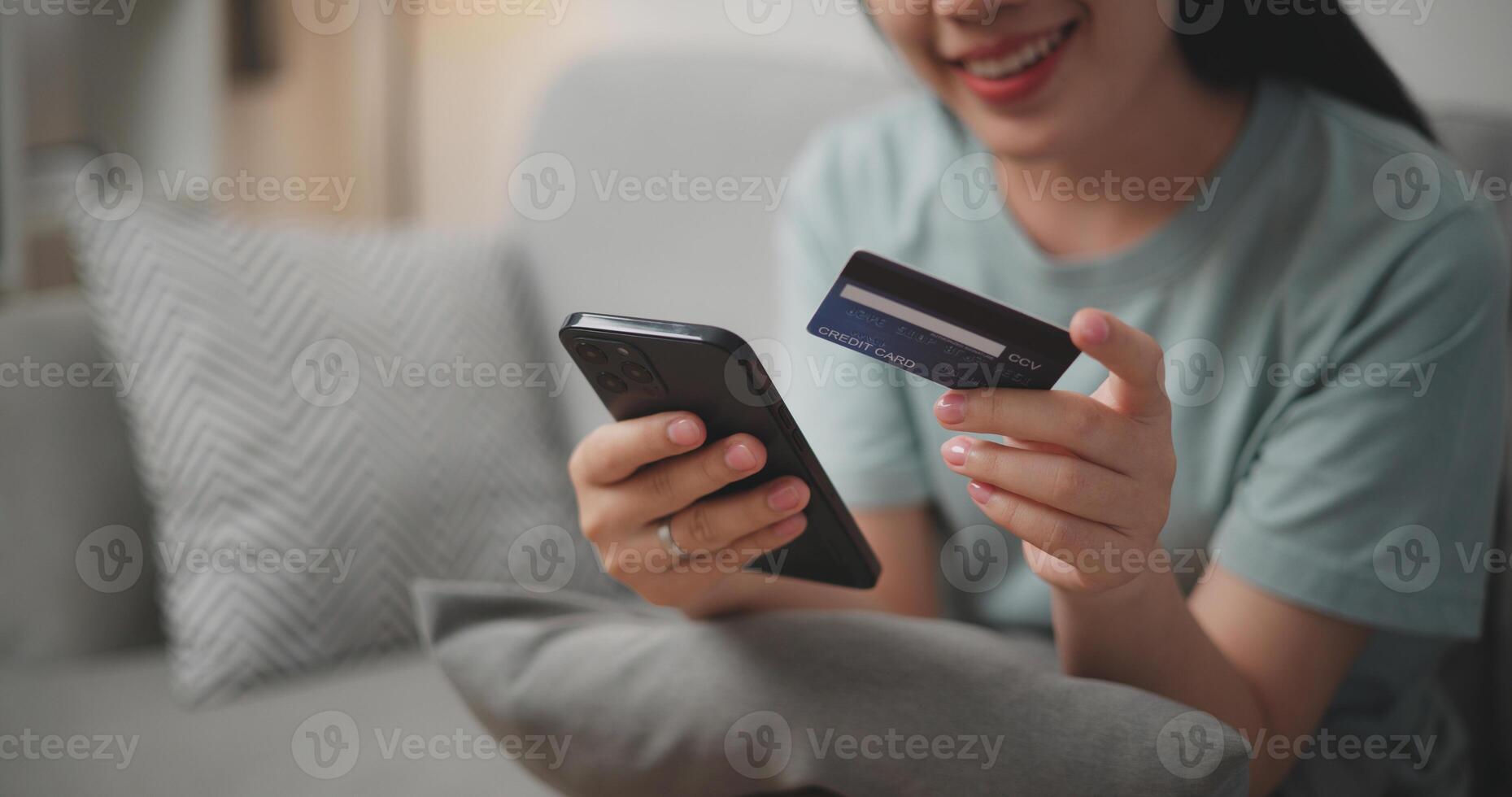 Selective focus, Hands of Young asian woman sitting on sofa holding credit card making online payment for purchase in web store using smartphone. photo