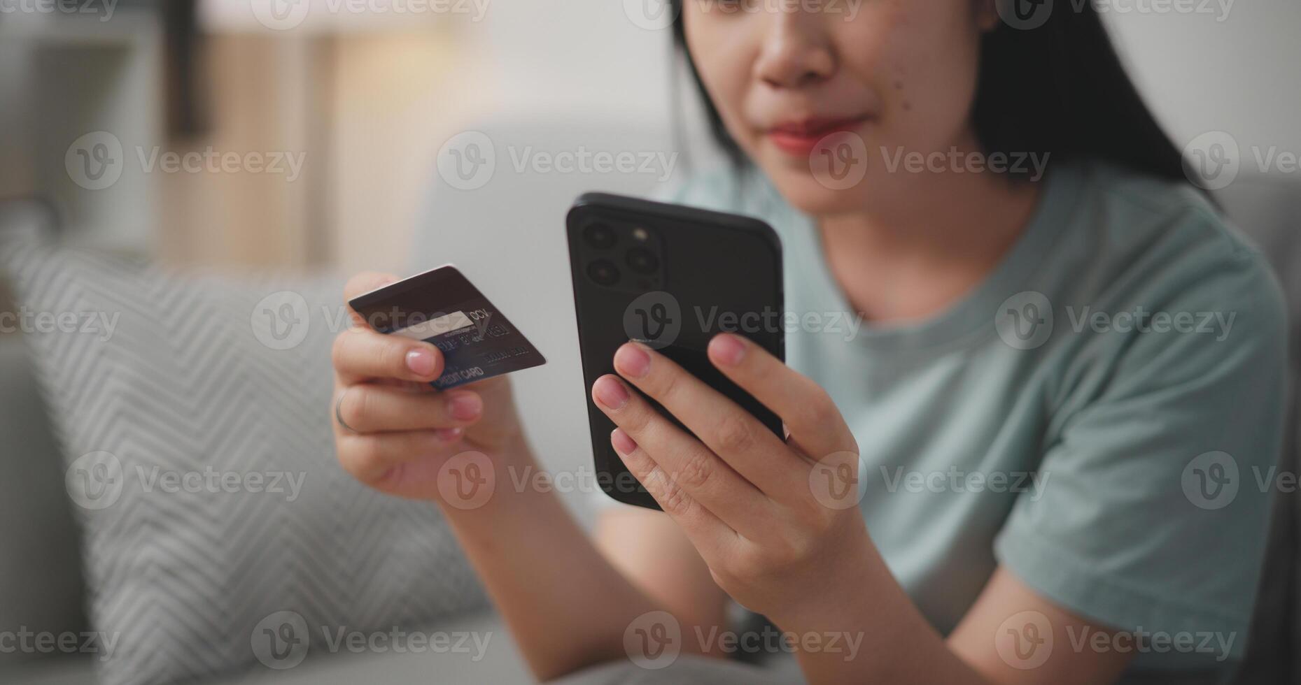 Selective focus, Hands of Young asian woman sitting on sofa holding credit card making online payment for purchase in web store using smartphone. photo