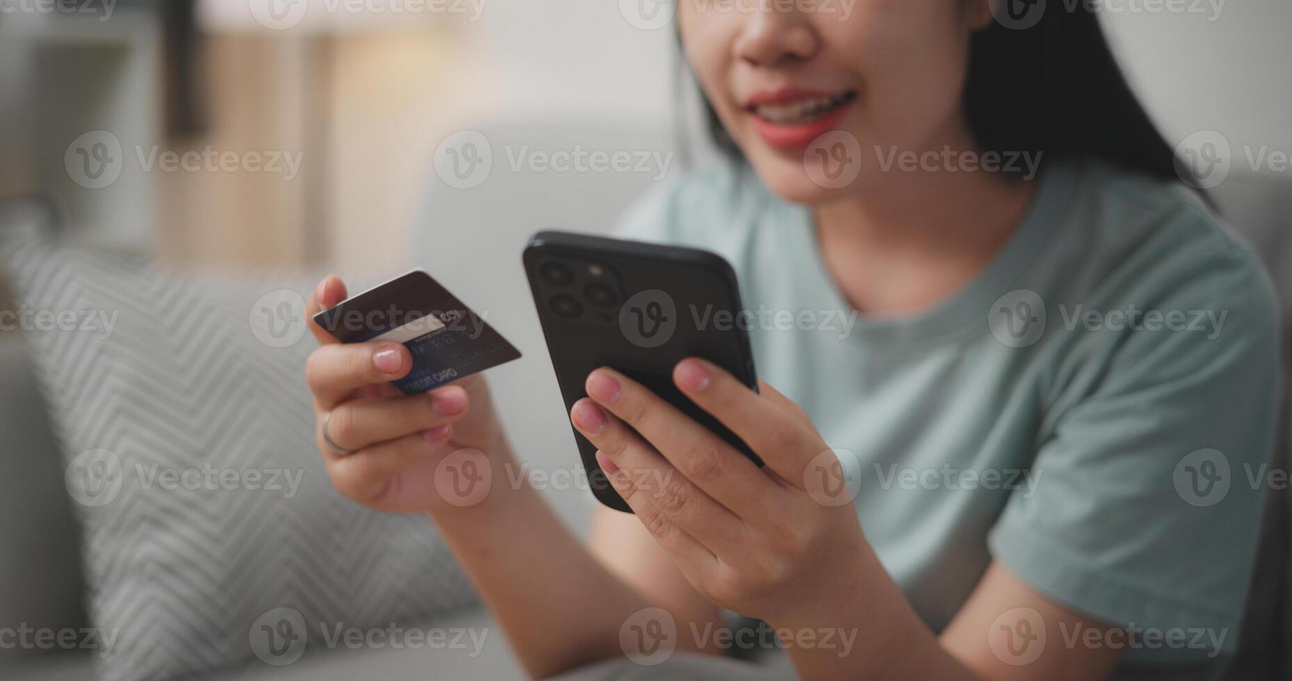 Selective focus, Hands of Young asian woman sitting on sofa holding credit card making online payment for purchase in web store using smartphone. photo