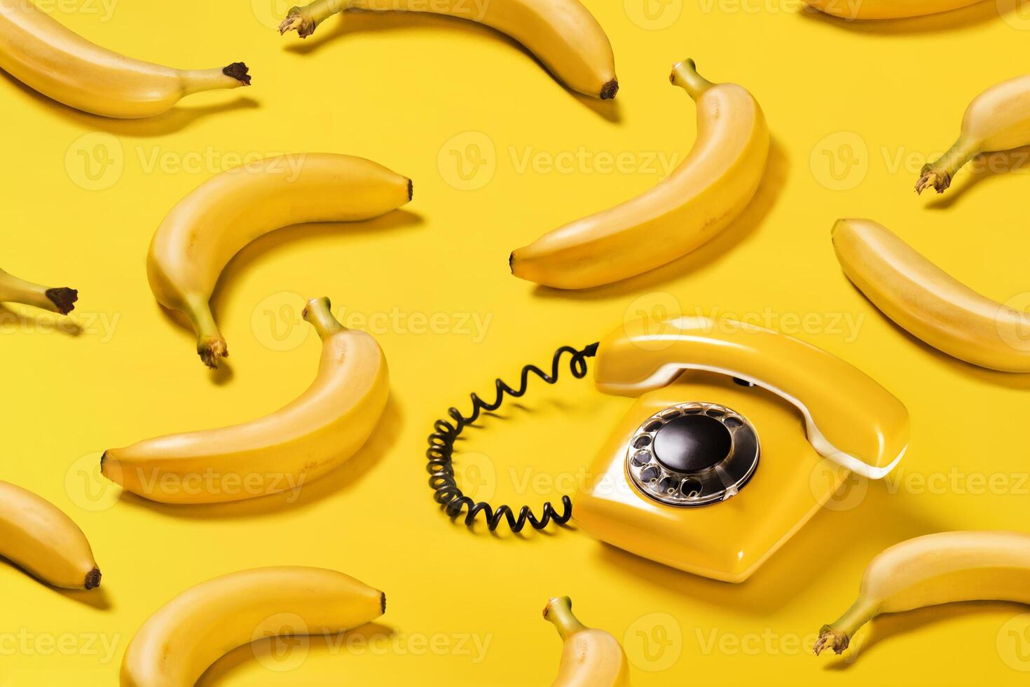 Creative pattern bananas and old yellow phone with hard shadows pattern on yellow background flat lay photo