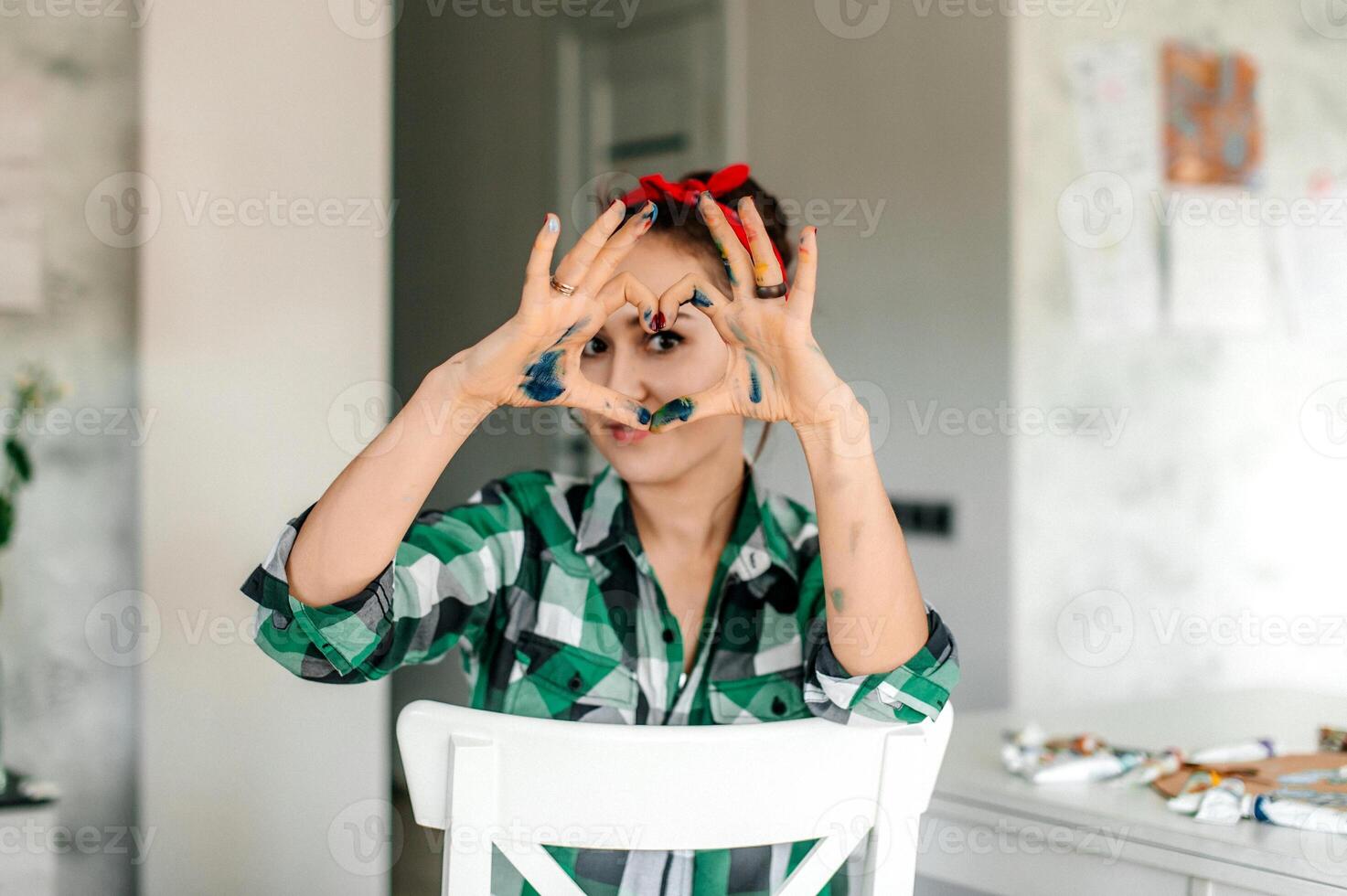 Woman with paint on her hands making heart shape with fingers. photo