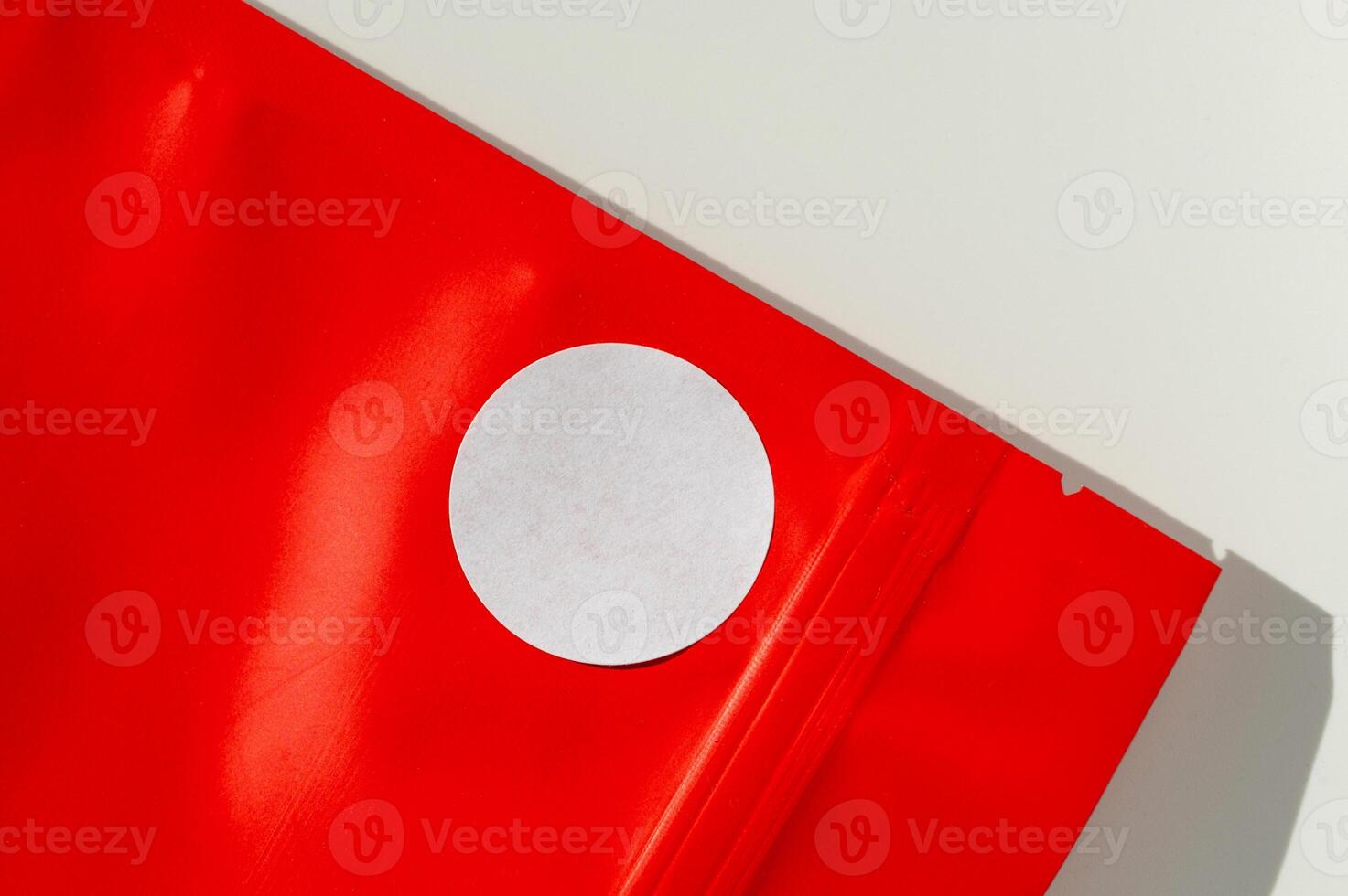 White circular sticker on red poly mailer envelope with natural shadow. photo