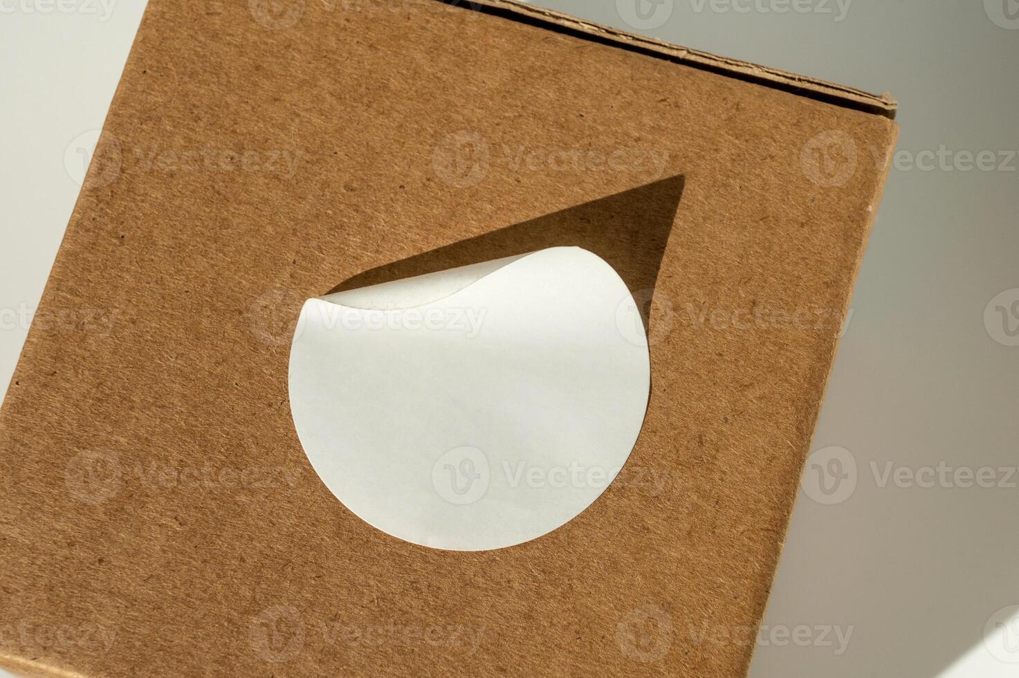 marrón cartulina caja con circular blanco pegatina en un neutral antecedentes. foto