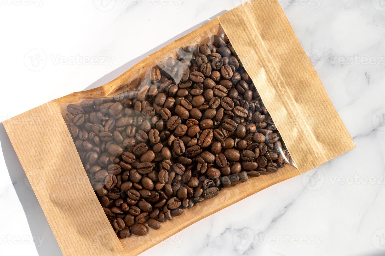 Coffee beans in transparent window pouches on brown paper bags. photo