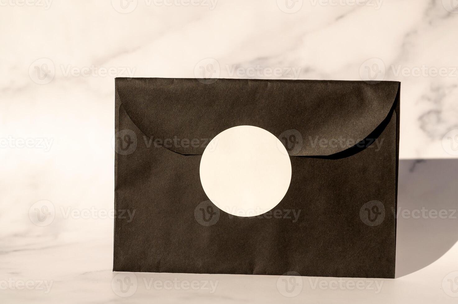 Black envelope with white circular label on marble background. photo