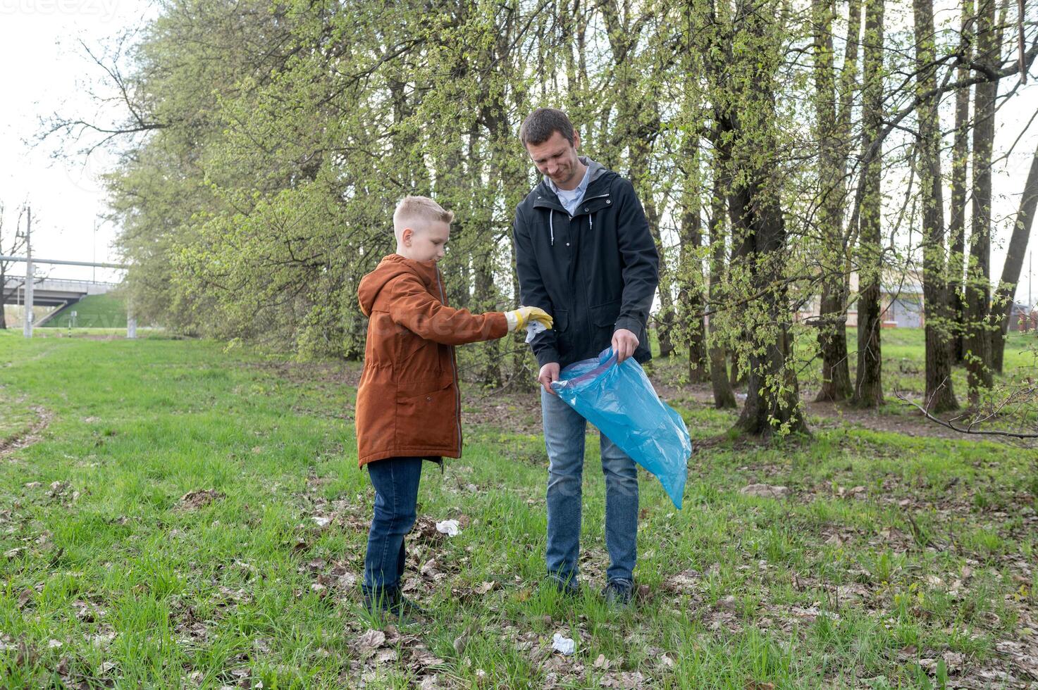 Father and son participating in a community clean-up, picking up litter in a park. photo