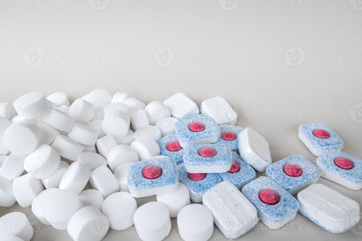 White pressed salt tablets and colored capsules with a red middle for a dishwasher close-up. photo