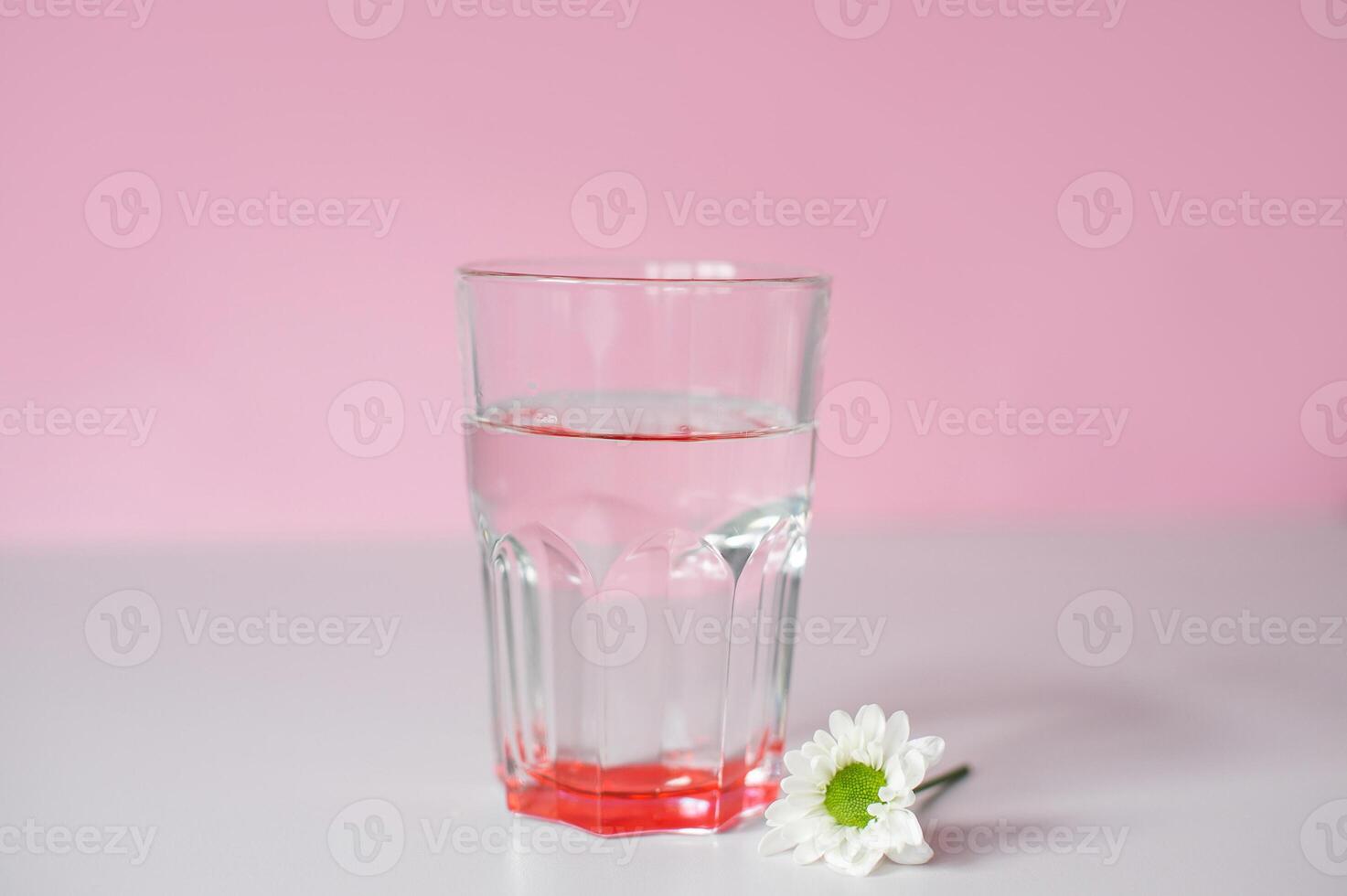 A transparent glass with drinking water stands on a pink background photo