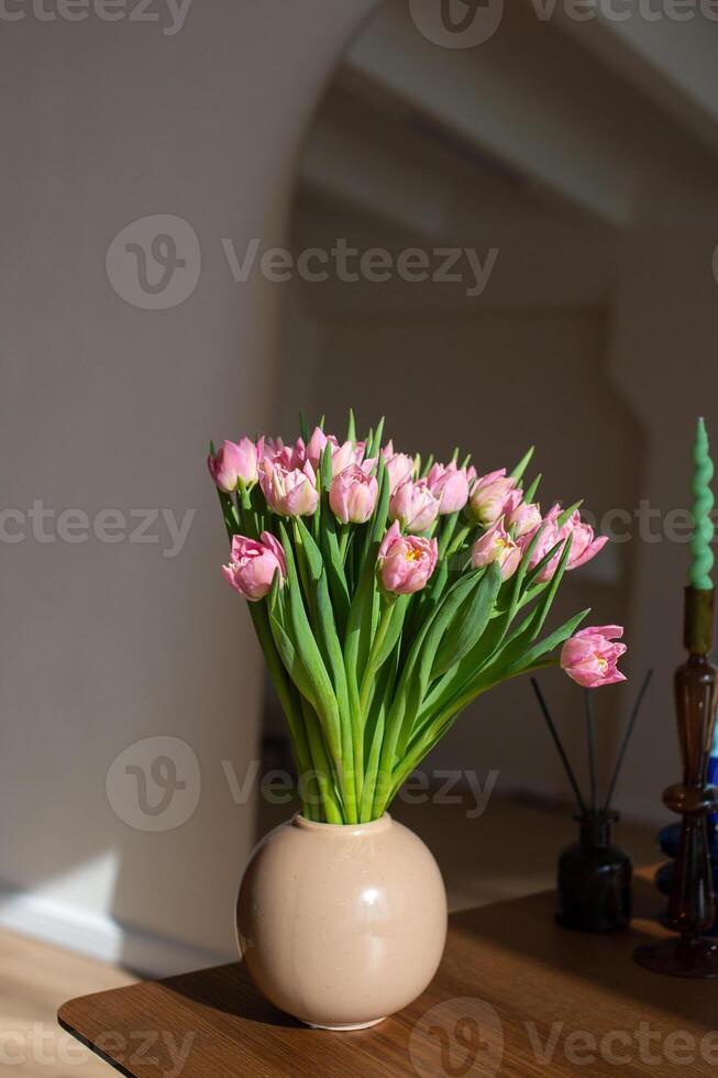 Pink tulips in a beige vase on a wooden table photo