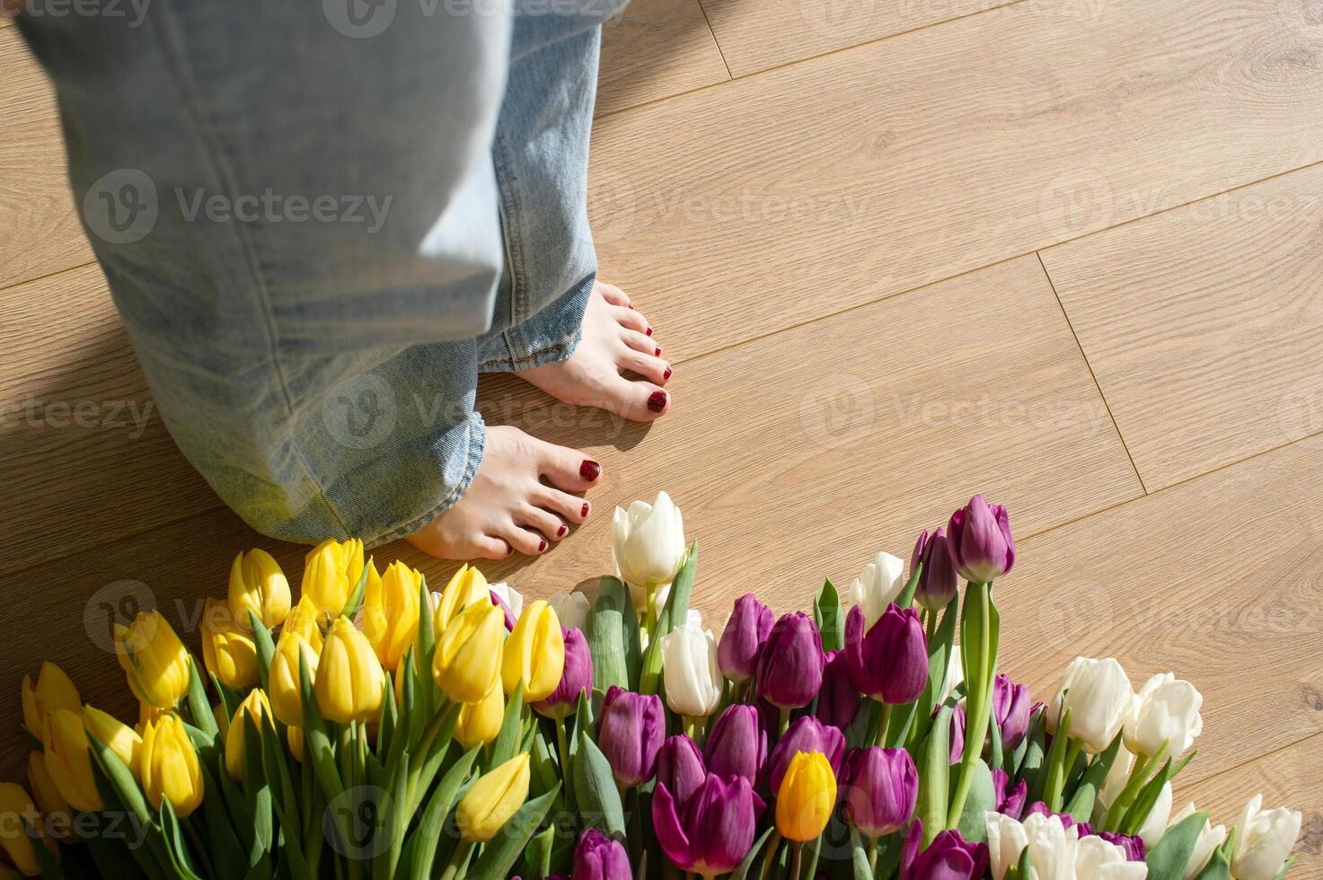 Close-up of woman's feet next to vibrant tulips bouquet on wooden floor. photo