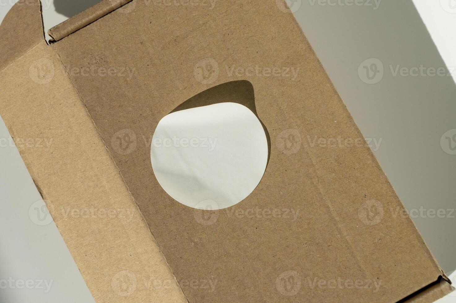 marrón cartulina caja con circular blanco pegatina en un neutral antecedentes. foto