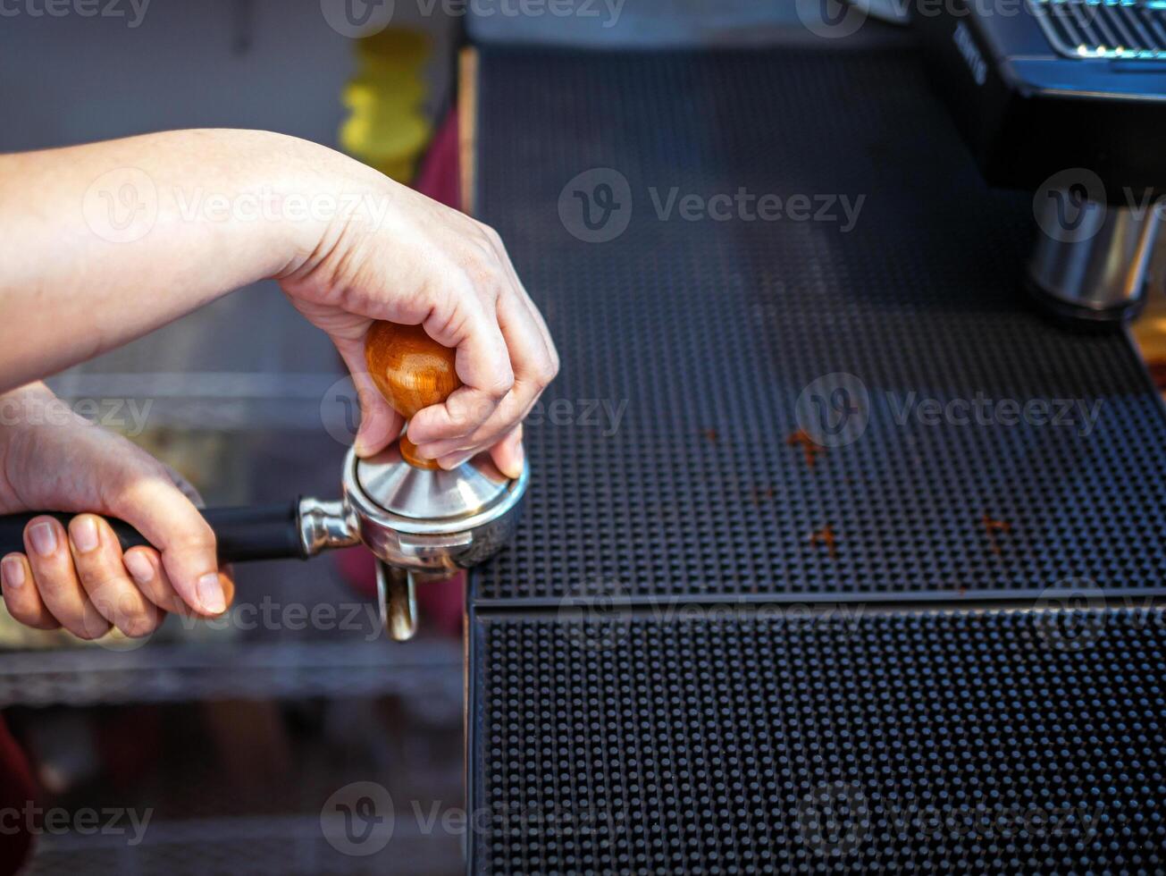 Hand of a barista holding a portafilter and a coffee tamper making an espresso coffee. Barista presses ground coffee using a tamper in a coffee shop photo