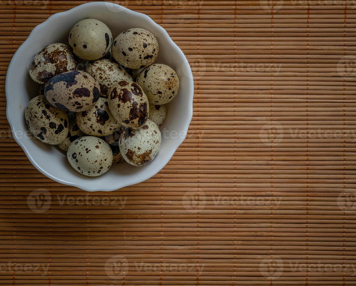 Fresh quail eggs in white plate on wooden black stone, selective focus photo