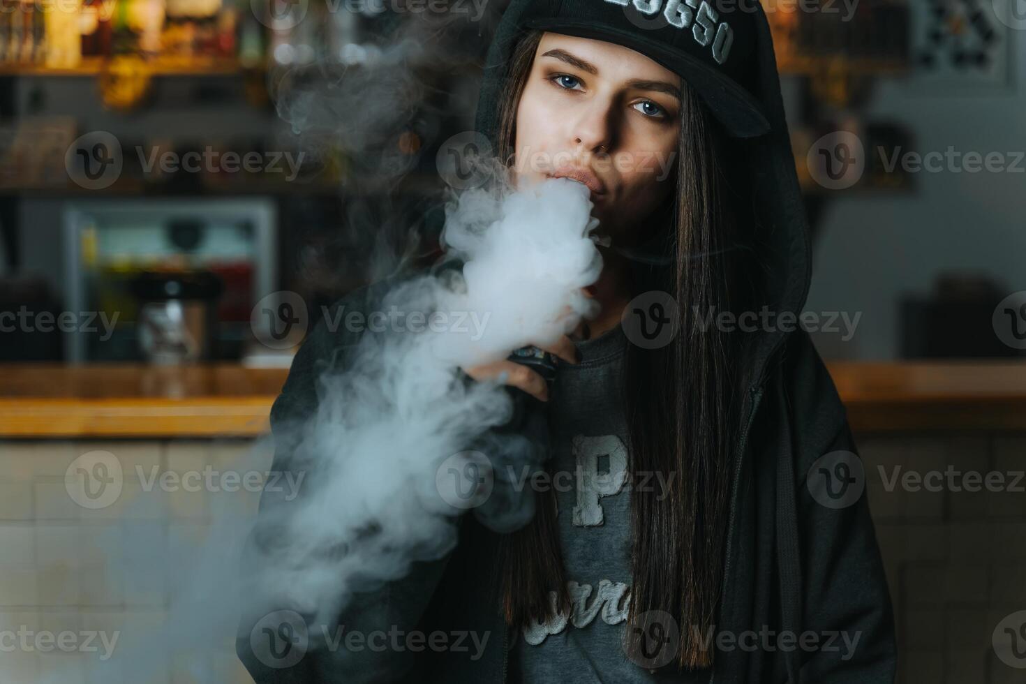 joven bonito mujer en gorra fumar un electrónico cigarrillo a el vape tienda. hip hop estilo. de cerca. foto