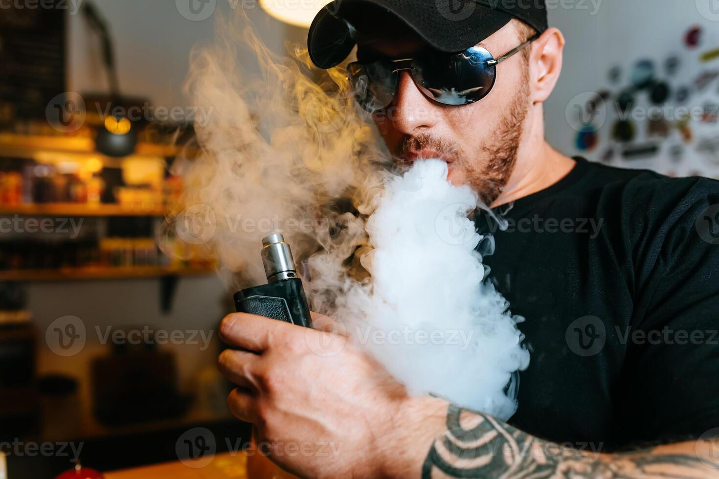brutal barbado hombre en Gafas de sol fumar un electrónico cigarrillo y lanzamientos nubes de vapor a el vape tienda. foto