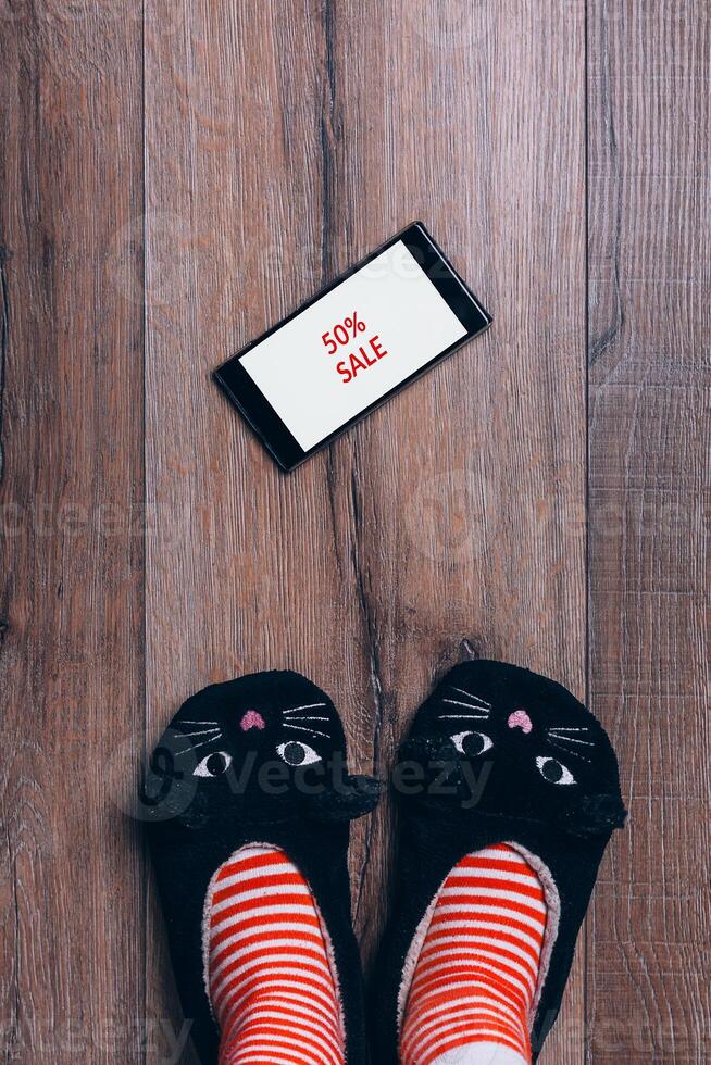 Smartphone on wooden wooden floor. Black friday advert. Woman feet in cat slippers, striped socks. Top view. online shopping concept. photo