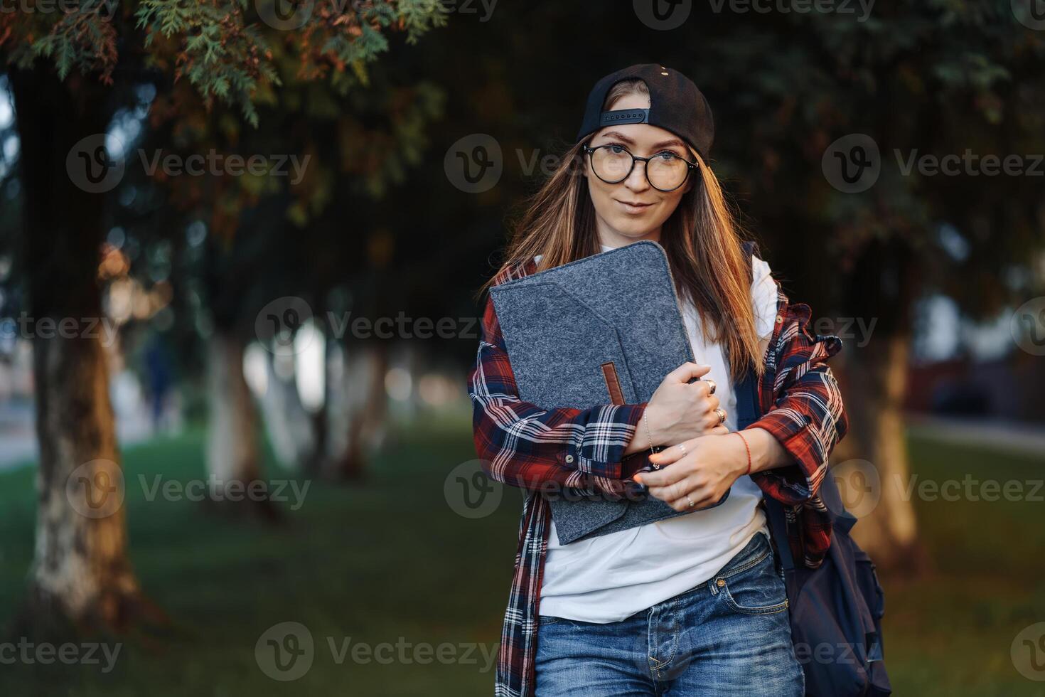 contento joven hembra estudiante vestido en casual ropa con taza de café y mochila detrás su espalda caminando alrededor ciudad. mujer estudiante participación ordenador portátil y Bebiendo café. verano puesta de sol tiempo. foto