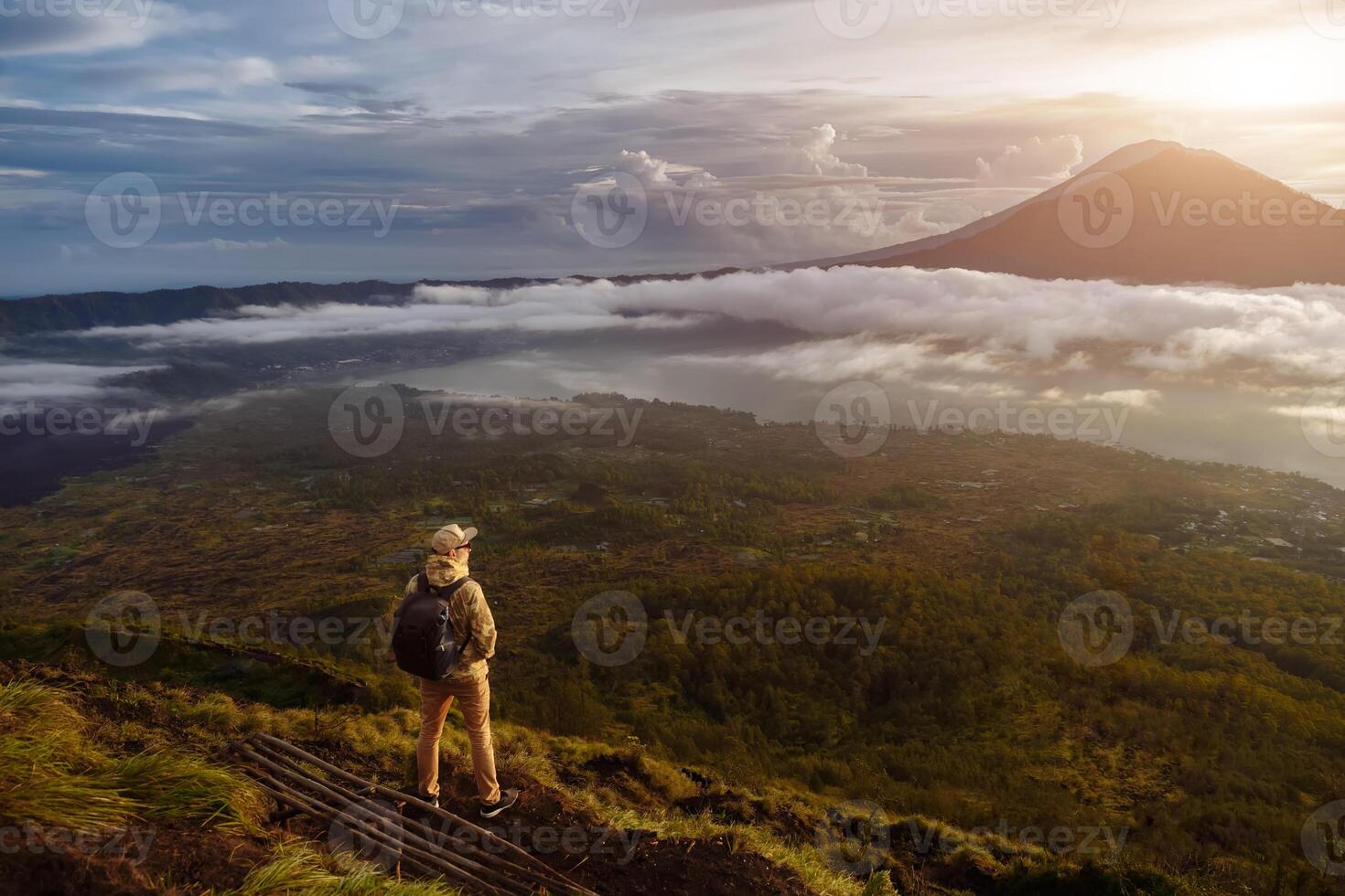 Man tourist looks at the sunrise on the volcano Batur on the island of Blai in Indonesia. Hiker man with backpack travel on top volcano, travel concept photo
