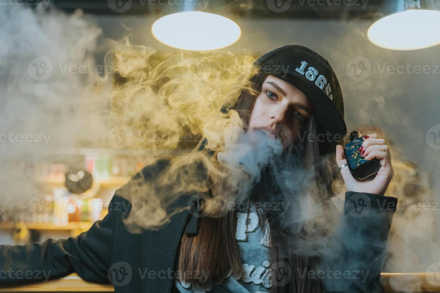 Young pretty woman in cap smoke an electronic cigarette at the vape shop. Hip-hop style. Closeup. photo