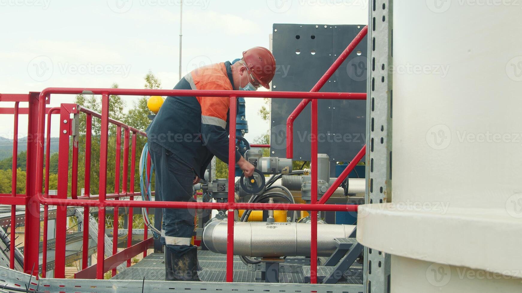 Employee of the gas station in a protective medical mask, gas distribution station turns or unscrews the gas supply valve. Work of a gas production worker at a gas station. photo