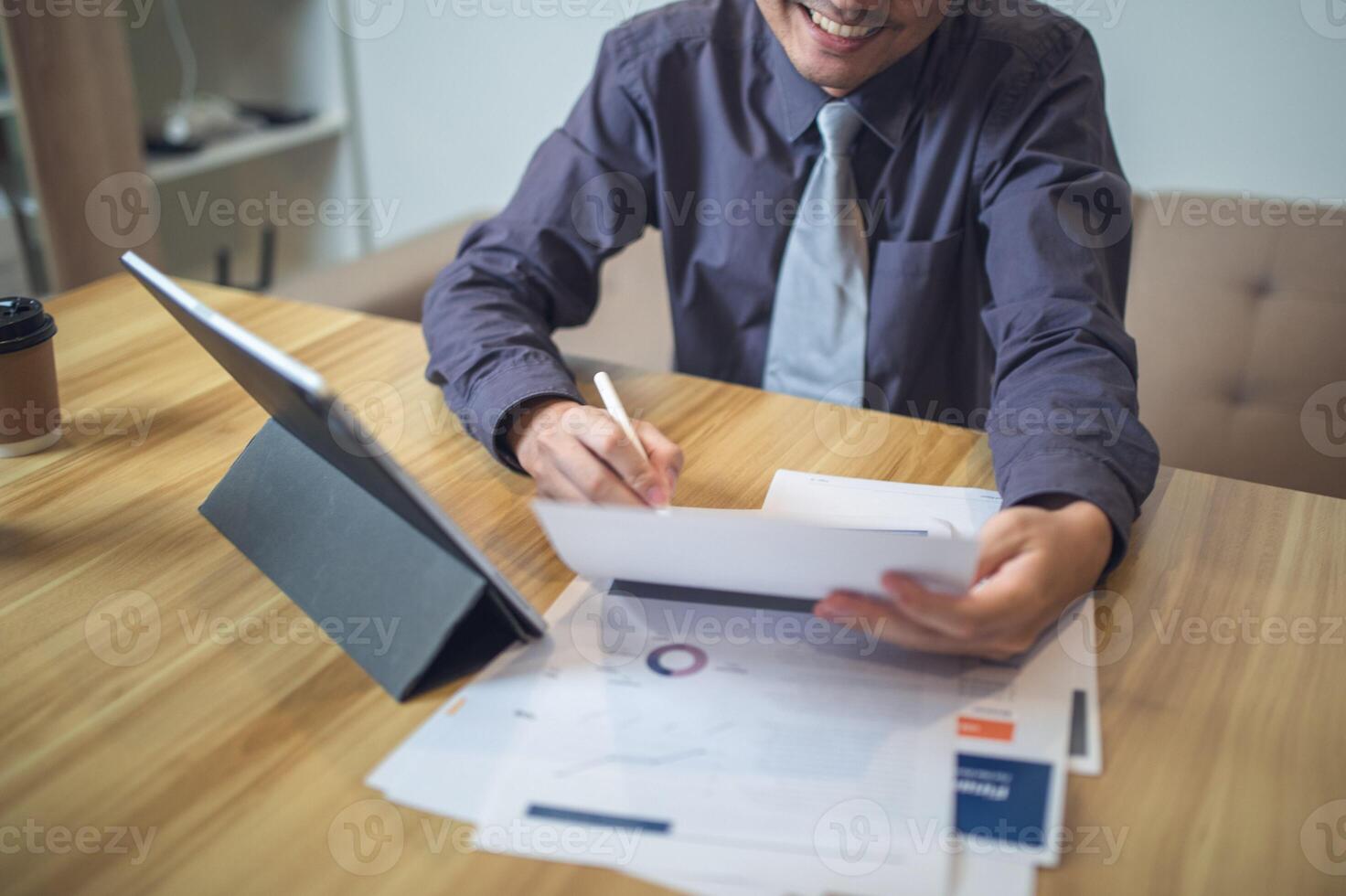 Businessman analyzing bar graph data with pen in hand, laptop and coffee on desk. Business concept photo