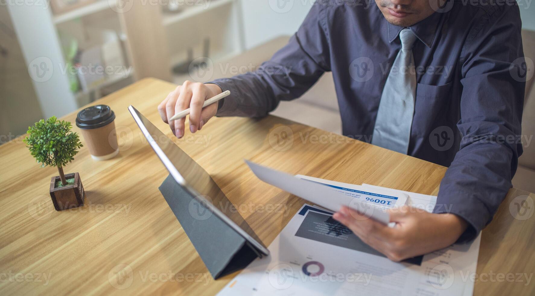 Businessman analyzing bar graph data with pen in hand, laptop and coffee on desk. Business concept photo