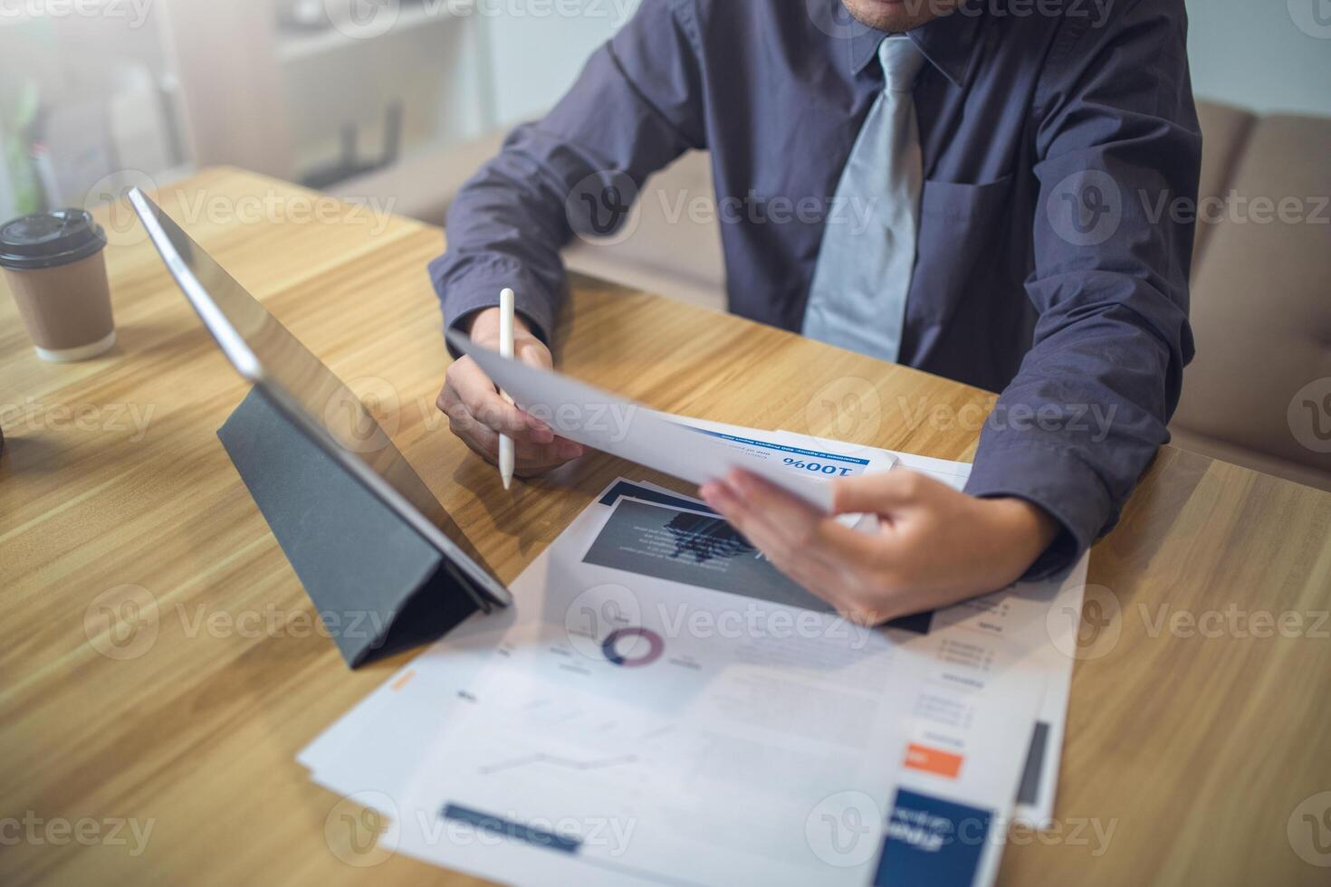 Businessman analyzing bar graph data with pen in hand, laptop and coffee on desk. Business concept photo