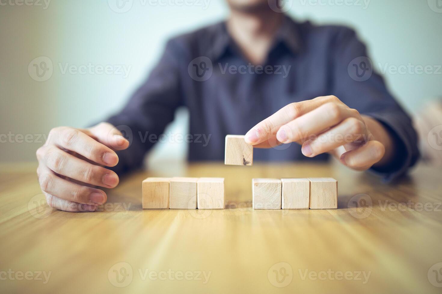 Hand strategically placing wooden blocks in a stair-step design on a table, signifying progressive success and growth photo