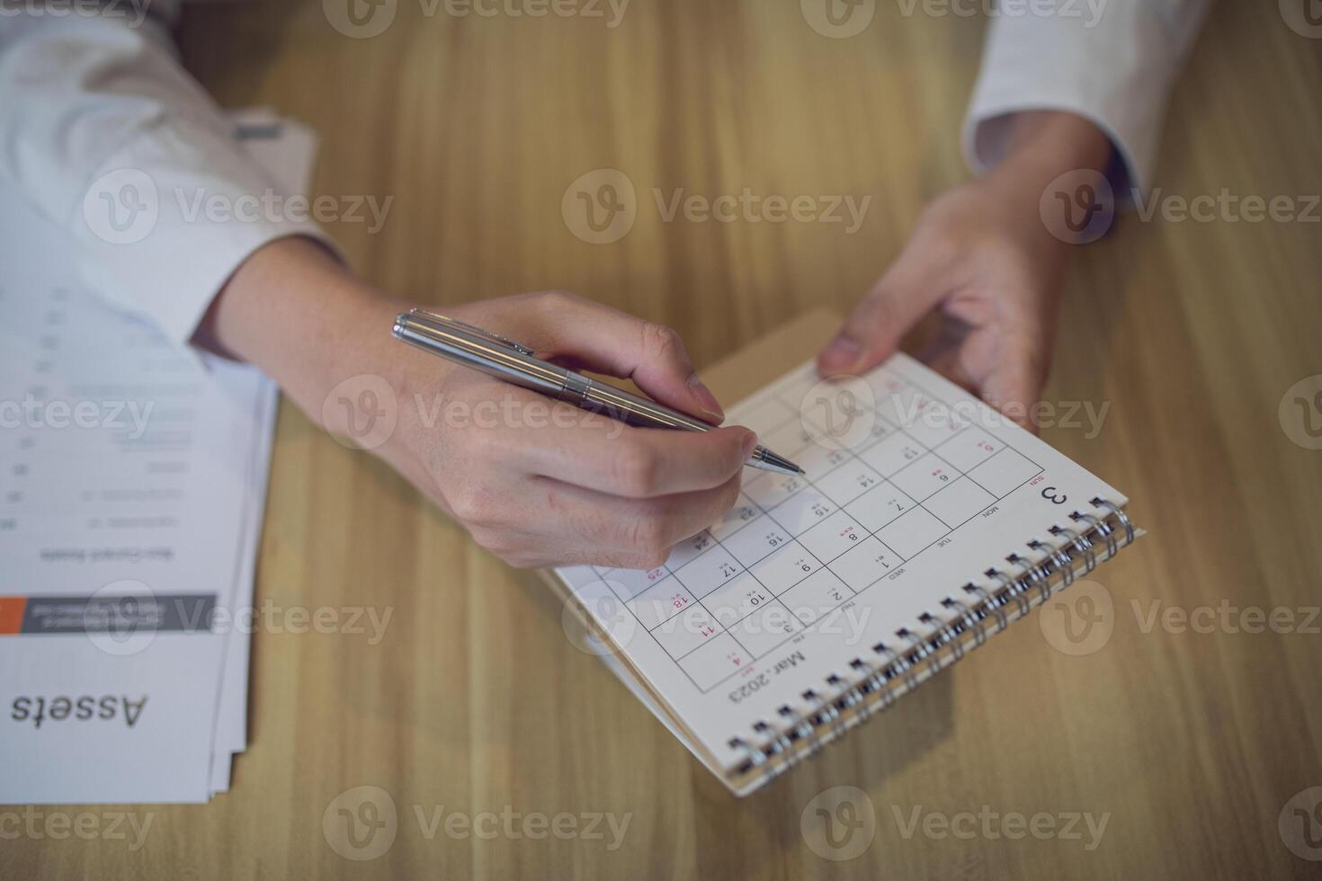 Professional setting a schedule in a planner with a pen, amidst a business-focused workspace photo