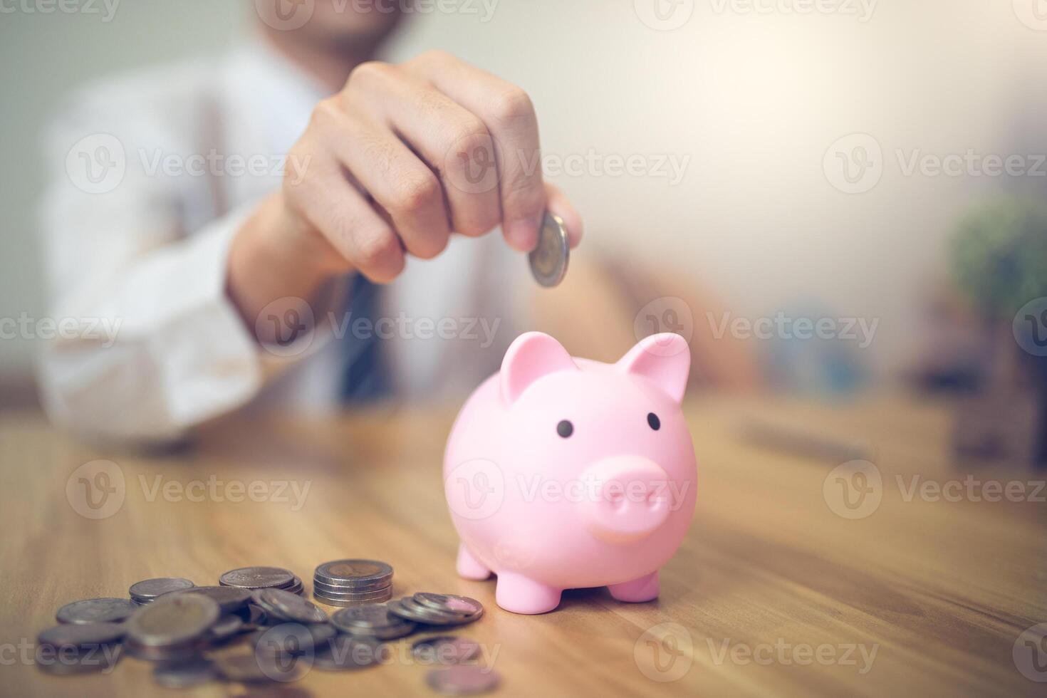 Person in a business shirt saving money in a piggy bank, with coins and financial reports on the table. Saving money business concept photo