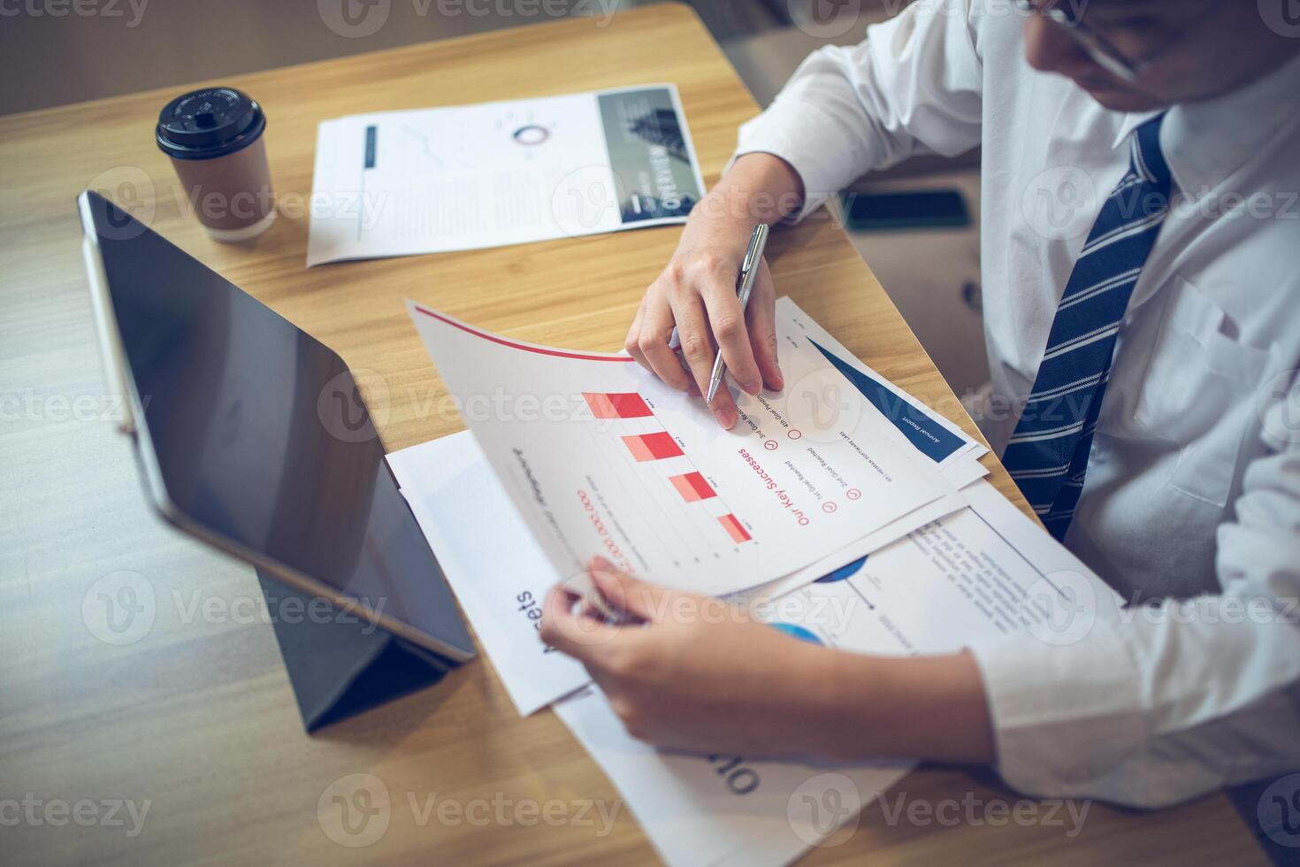 Businessman analyzing bar graph data with pen in hand, laptop and coffee on desk. Business concept photo