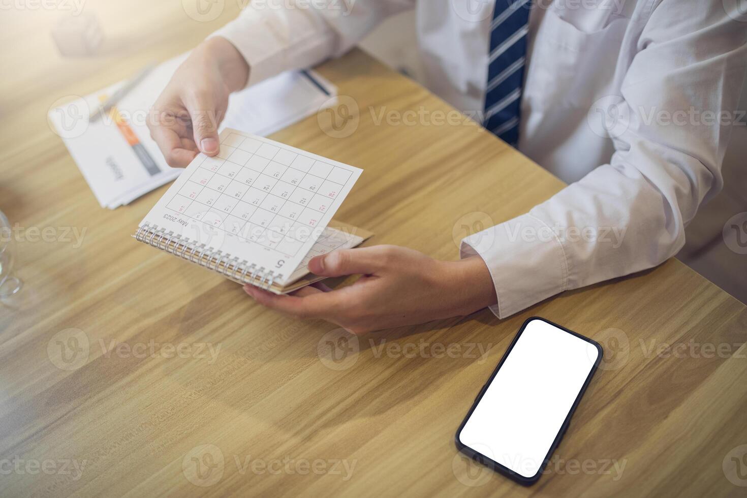 profesional en un blanco camisa Planificación en un diario con un teléfono inteligente con pantalla Bosquejo en el escritorio para rápido acceso foto