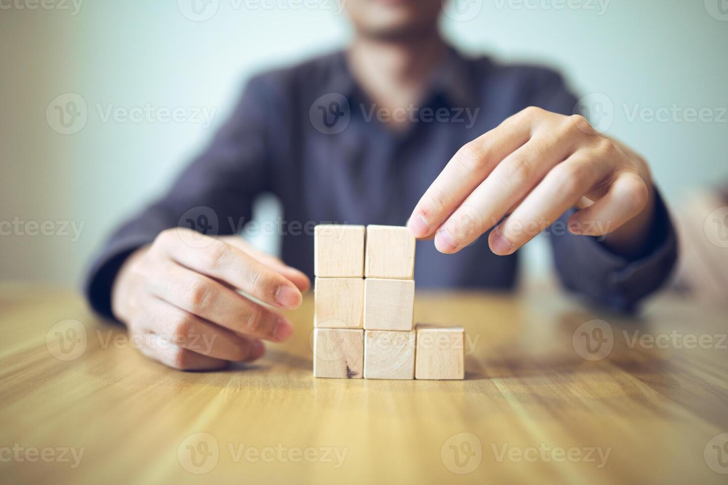 Hand strategically placing wooden blocks in a stair-step design on a table, signifying progressive success and growth photo