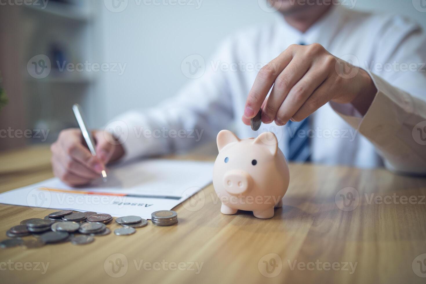 persona en un negocio camisa ahorro dinero en un cerdito banco, con monedas y financiero informes en el mesa. ahorro dinero negocio concepto foto