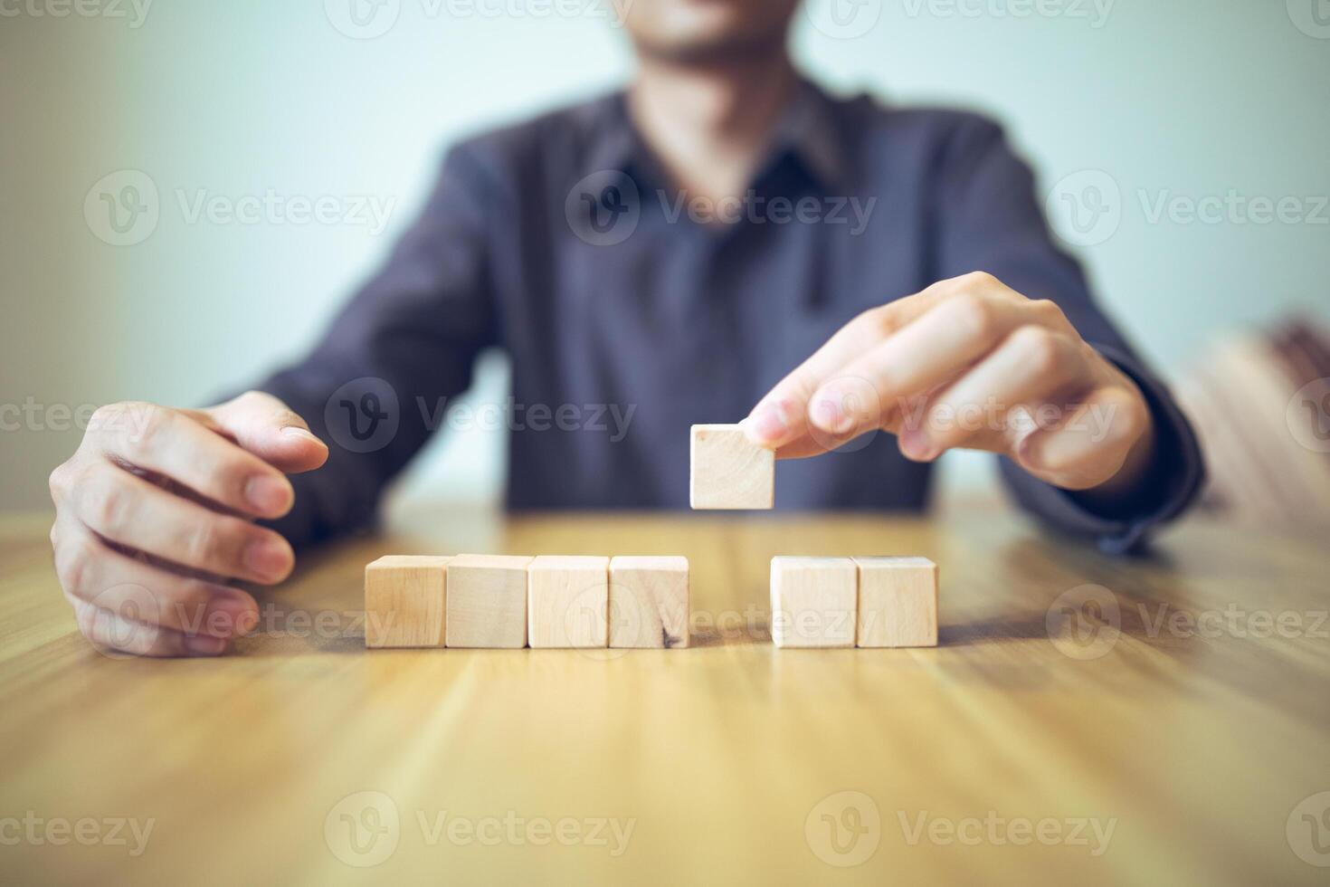 Hand strategically placing wooden blocks in a stair-step design on a table, signifying progressive success and growth photo