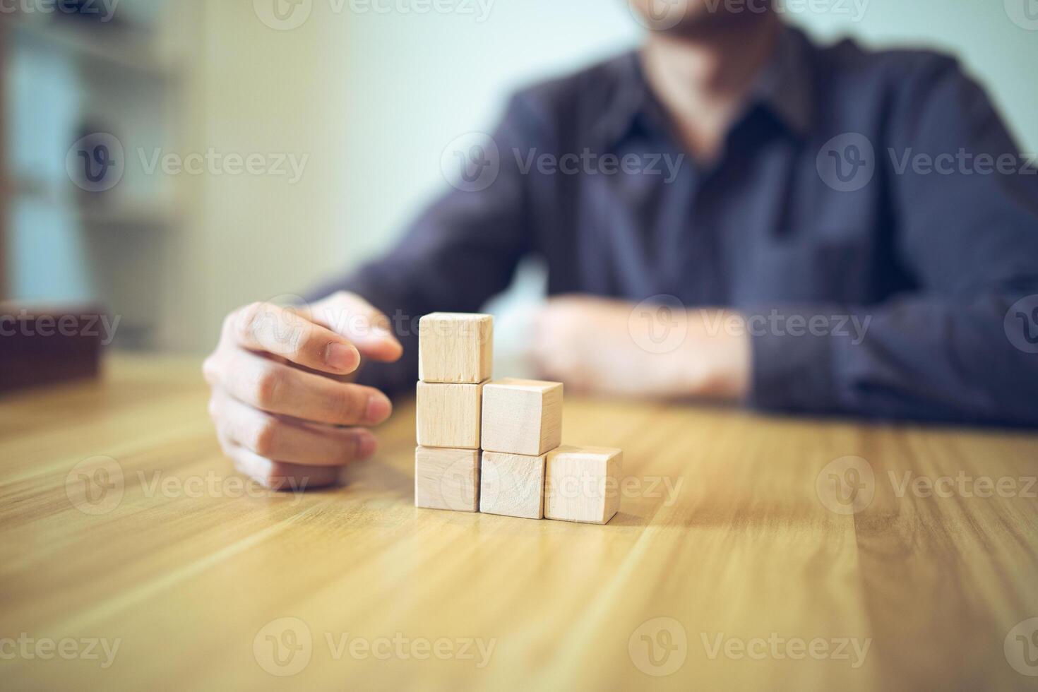 mano estratégicamente colocación de madera bloques en un escalón diseño en un mesa, significando progresivo éxito y crecimiento foto