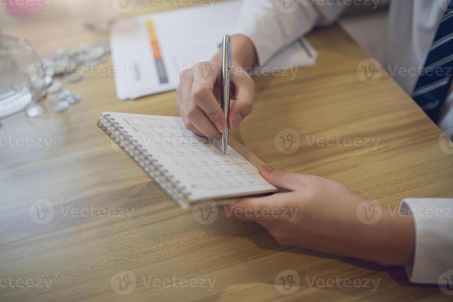 Professional setting a schedule in a planner with a pen, amidst a business-focused workspace photo