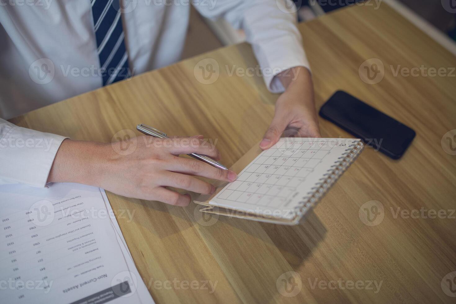 profesional ajuste un calendario en un planificador con un bolígrafo, en medio de un centrado en los negocios espacio de trabajo foto