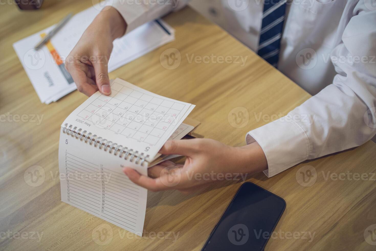 Professional setting a schedule in a planner with a pen, amidst a business-focused workspace photo