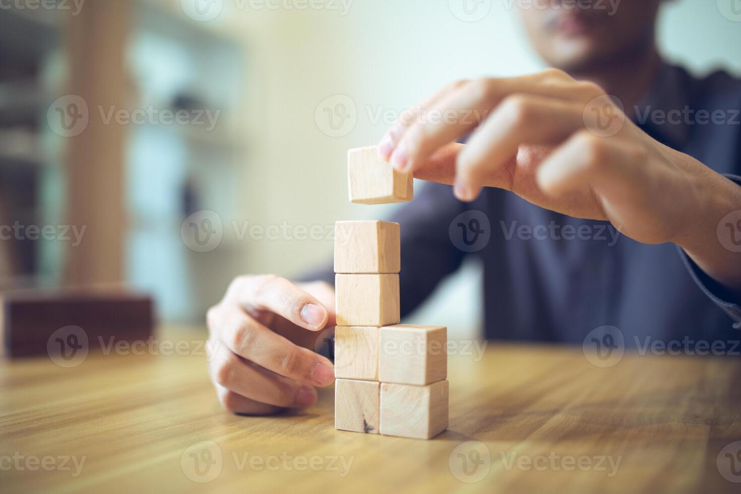 Hand strategically placing wooden blocks in a stair-step design on a table, signifying progressive success and growth photo