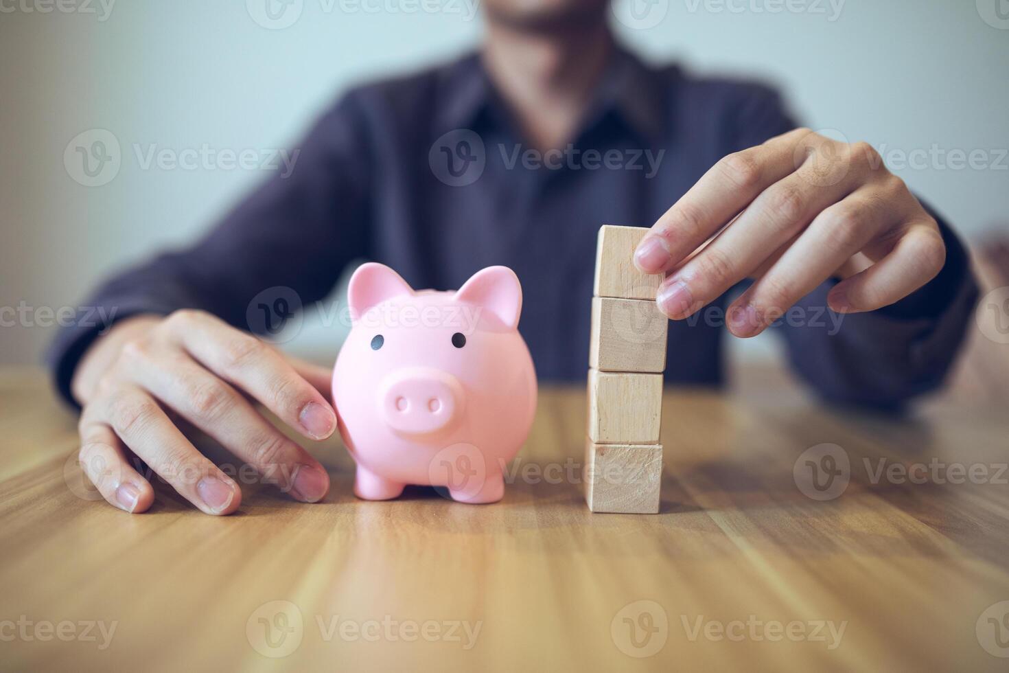 Person building a tower from wooden blocks beside a piggy bank, symbolizing financial planning and saving photo