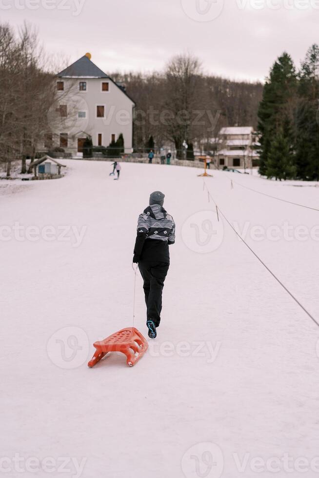 Woman with a sled on a rope walks along the top of a hill. Back view photo