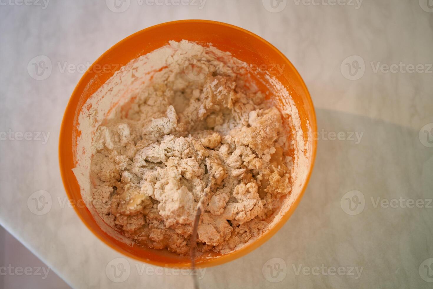 Spoon sharpens from a bowl with kneaded dough on the table. Top view photo