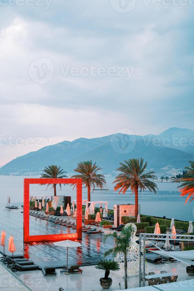 Illuminated red square arch stands in a long pool by the sea. Porto, Montenegro photo