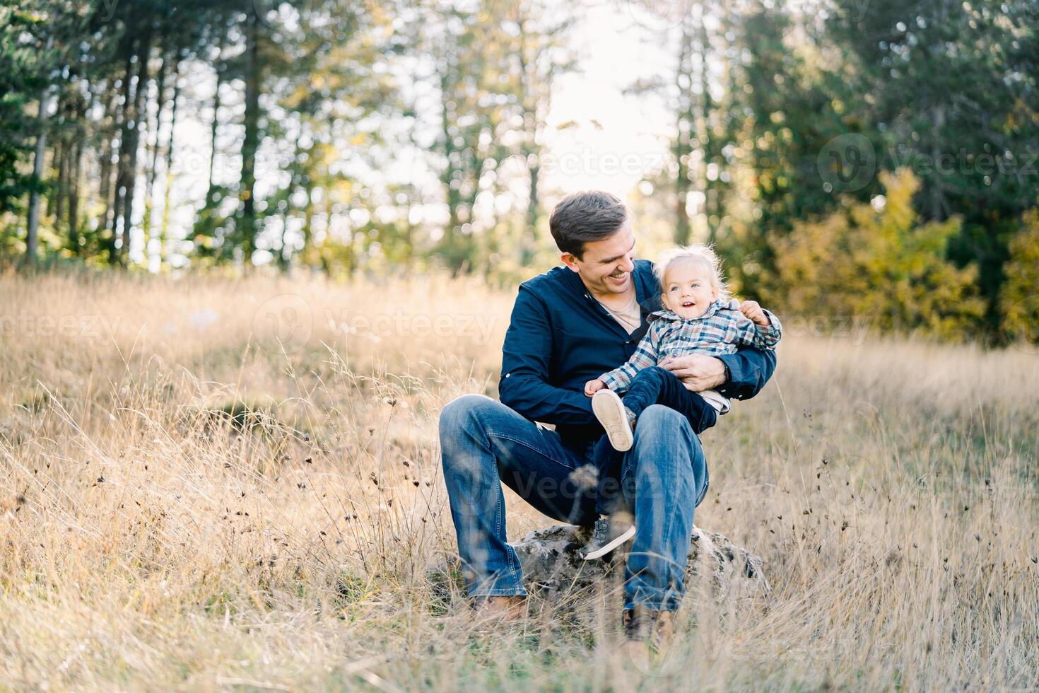 Laughing dad hugging a little girl, sitting on his knees on the lawn photo