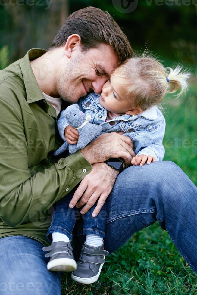 Smiling dad hugs a little girl in his arms, resting his head on her shoulder photo