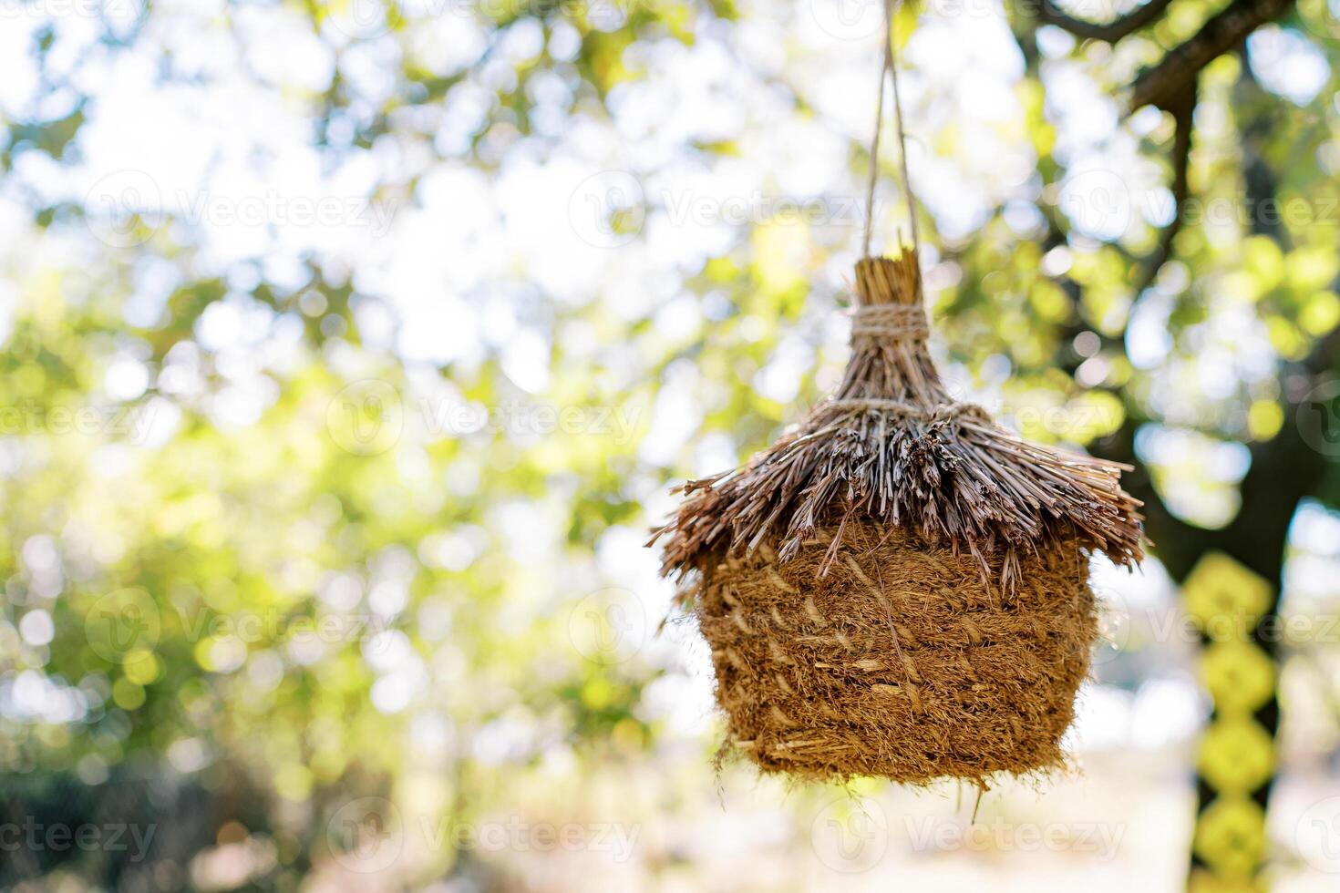 Wicker straw bird nest hanging on a rope on a tree in the park photo