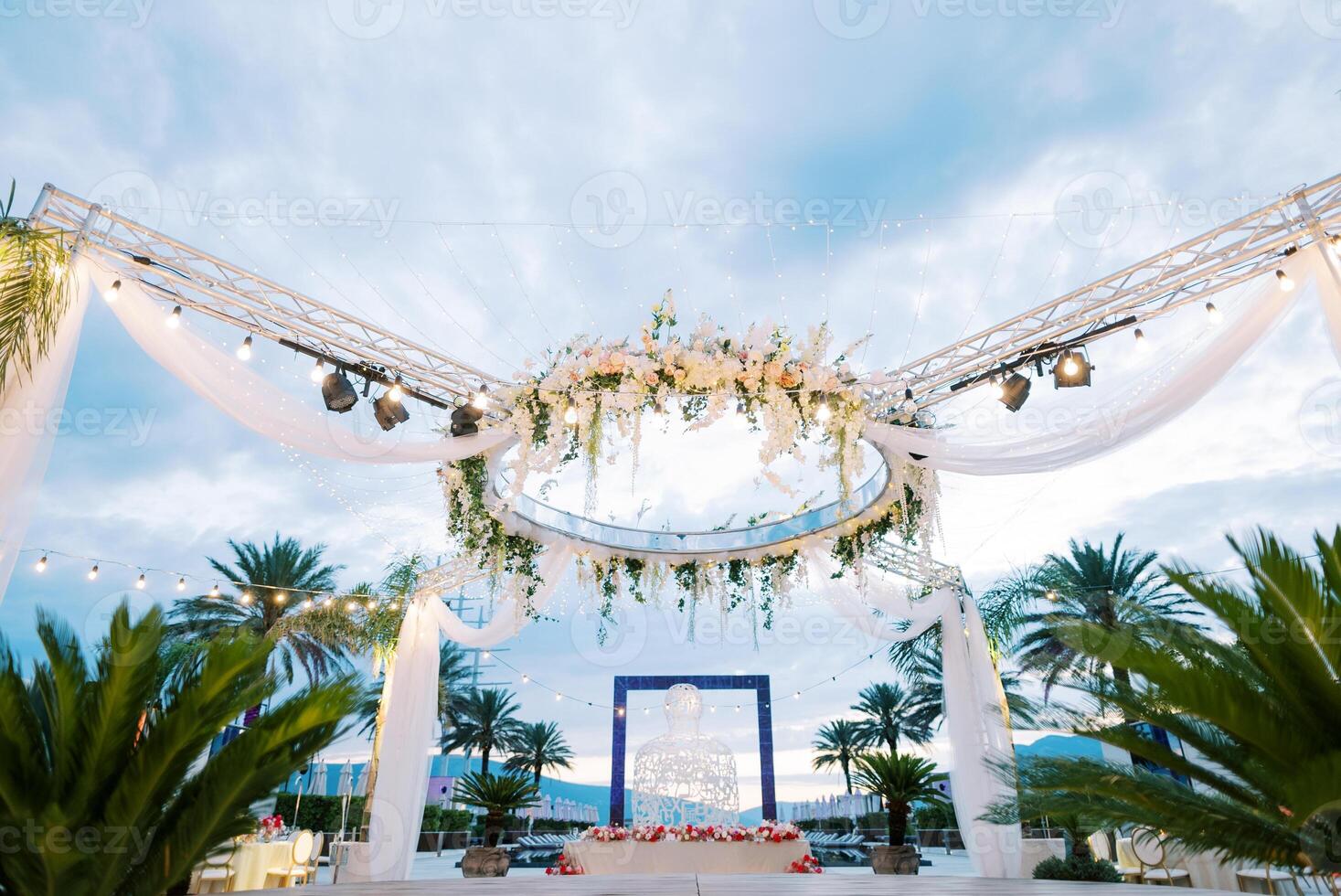 Round stand with spotlights decorated with flowers and white fabric above a laid festive table photo