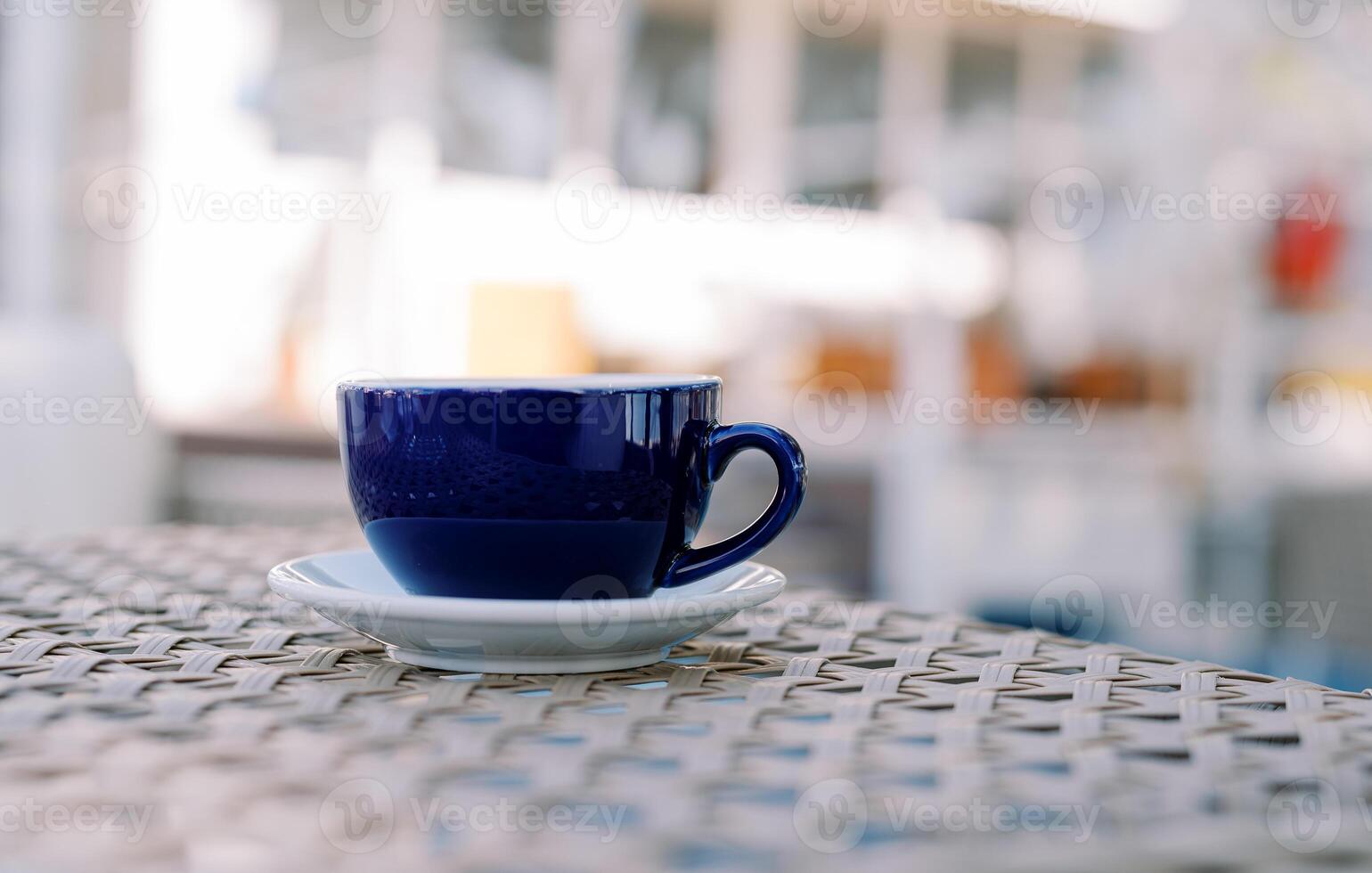 Latte in a cup on a saucer stands on a wicker table in an outdoor cafe photo